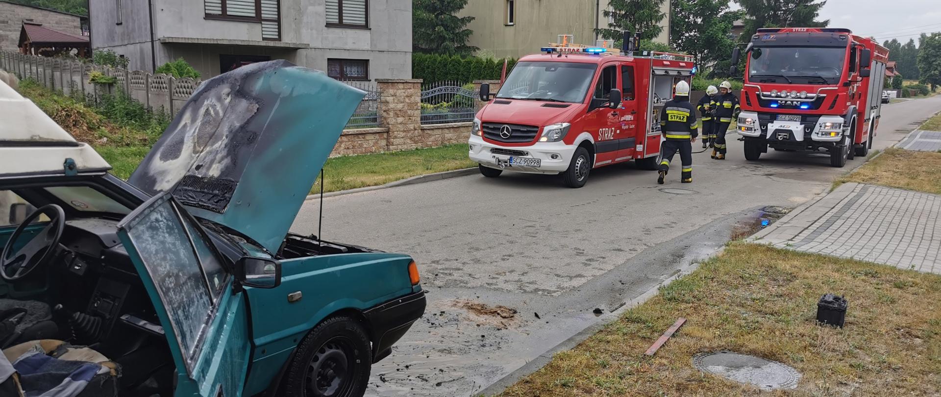 Wąsosz - pożar samochodu - z lewej strony samochód osobowy po pożarze, za nim strażacy i samochody gaśnicze