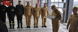 uroczysta zmiana służby w garażu Jednostki Ratowniczo Gaśniczej PSP w Brzezinach . na pierwszym planie komendanci komendy PSP w Brzezinach dalej funkcjonariusze biura oraz JRG stojący na baczność