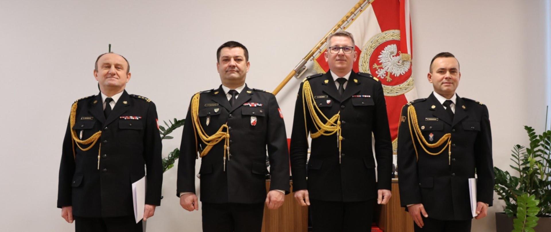 Na zdjęciu gabinet komendanta głównego PSP. Od lewej w szeregu, mundurach wyjściowych stoją: odwołany ze stanowiska st. bryg. Bogdan Jędrocha, śląski komendant wojewódzki PSP nadbryg. Jacek Kleszczewski, zastępca komendanta głównego PSP nadbryg. Krzysztof Hejduk, nowo powołany zastępca mł. kpt. Arkadiusz Krzemiński. W tle na ścianie sztandar KG PSP .