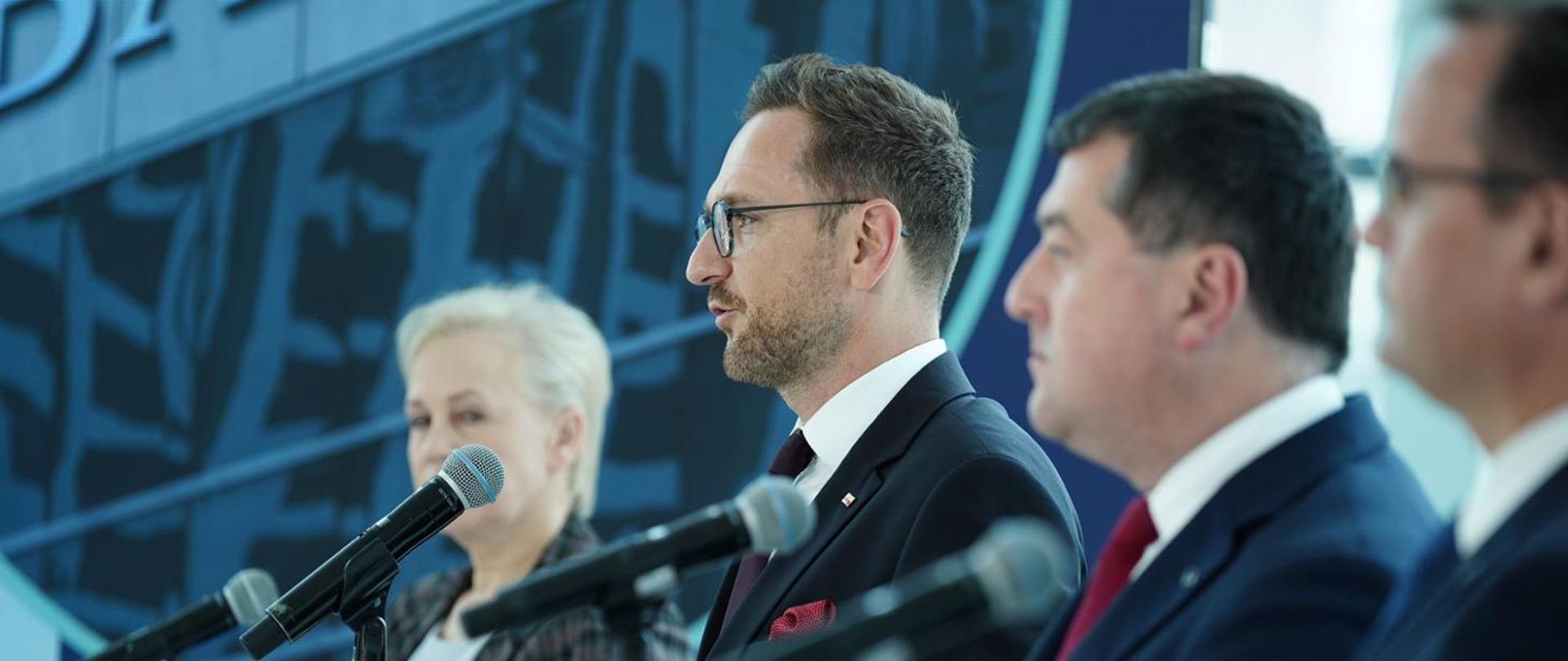 cztery osoby stoją i przemawiają do mikrofonów