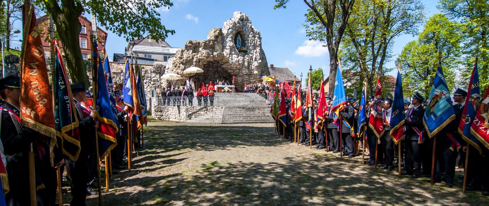 Pielgrzymka strażaków na Górę Świętej Anny. Strażacy w mundurach wyjściowych stoją ze sztandarami przed grotą na Górze Świętej Anny.