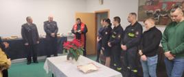 Zdjęcia przedstawiają strażaków z KP PSP Wołomin podczas spotkania wigilijnego w komendzie. Na zdjęciach widoczni są funkcjonariusze w mundurach wyjściowych oraz koszarowych. Pośród strażaków jest również ksiądz kapelan. Strażacy stoją wokoło stołu nakrytego białym obrusem na którym stoi opłatek. na innych zdjęciach widać strażaków dzielących się opłatkiem i skłądających sobie życzeniaz.