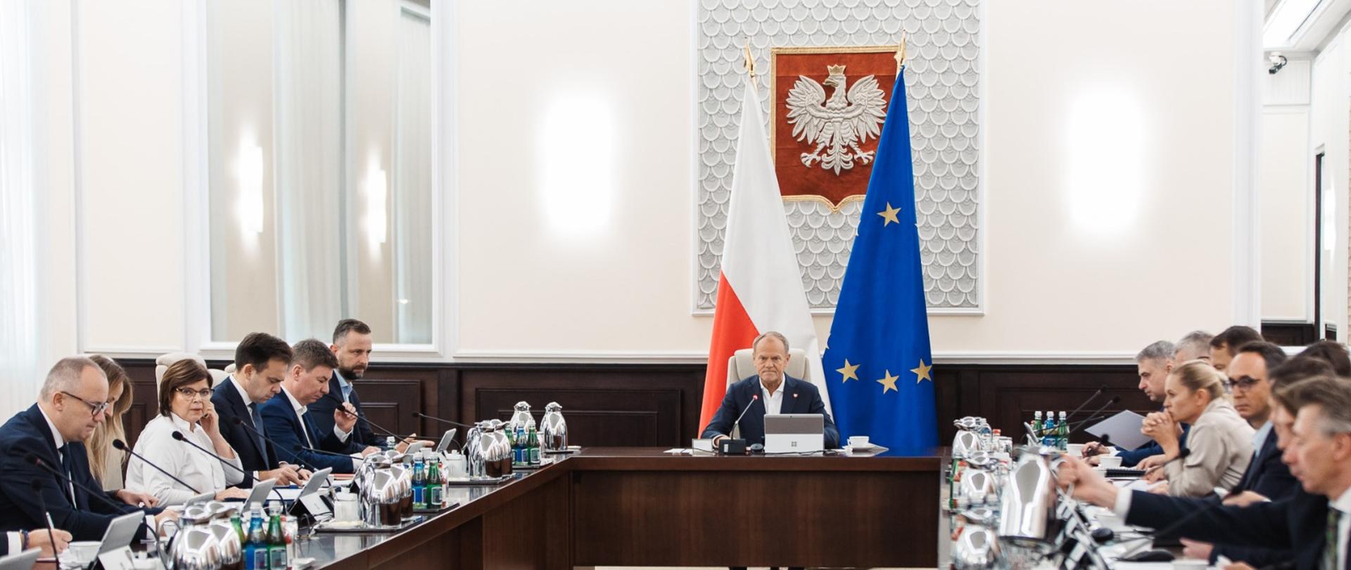 sala posiedzeń rady ministrów. po środku premier donald tusk, za nim flagi polski i ue. wokół stoły, przy których siedzą ministrowie.