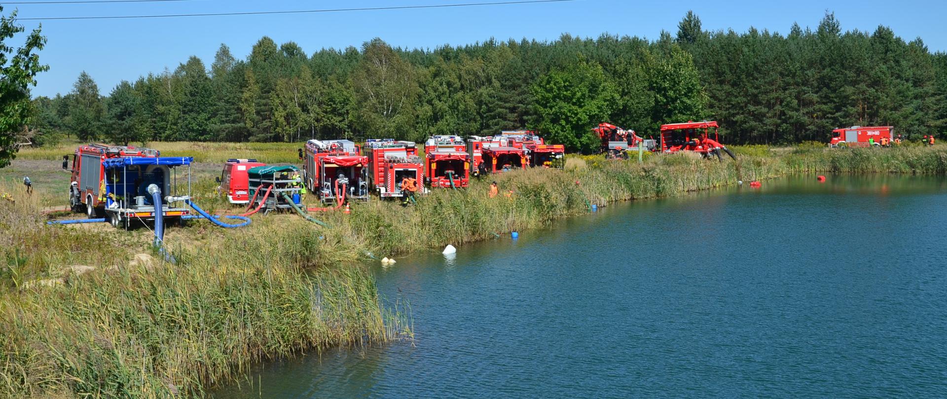 Przy zbiorniku wodnym widoczne ustawione duże pompy pożarnicze.