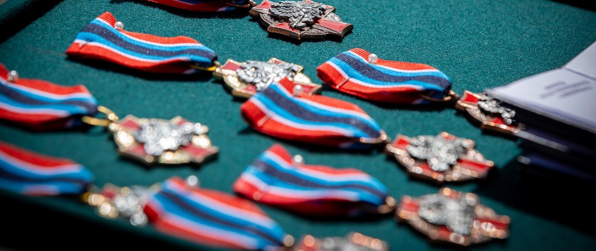 Na zielonym aksamicie ułożone odznaczenia – krzyże z niebiesko-czerwonymi wstążkami, gotowe do wręczenia wyróżnionym funkcjonariuszom.