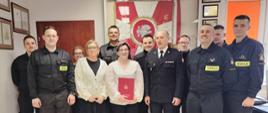 Zdjęcie przedstawia jubilatkę oraz pracowników i funkcjonariuszy na tle sztandaru KP PSPj