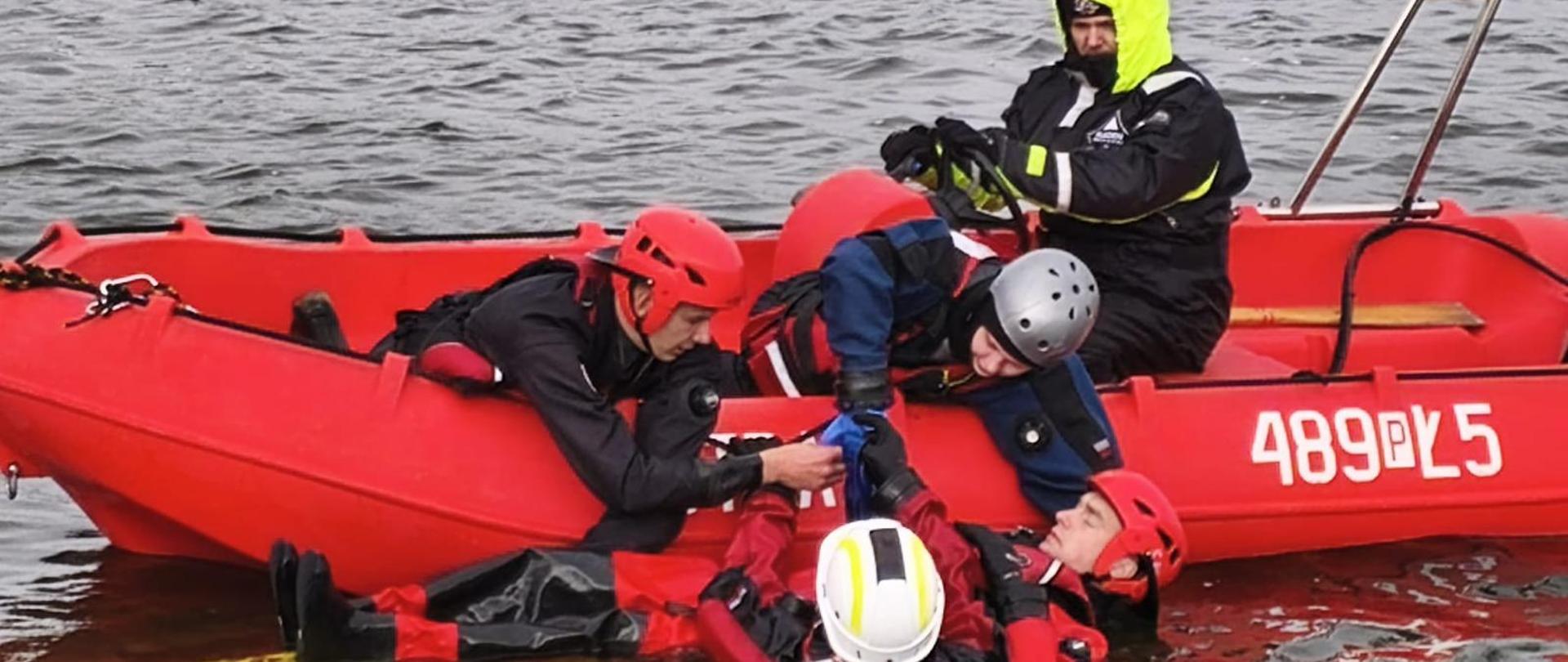 Na zdjęciu strażacy podczas szkolenia na jeziorze, strażacy na łodzi i w wodzie ćwiczą ratowanie osoby poszkodowanej.