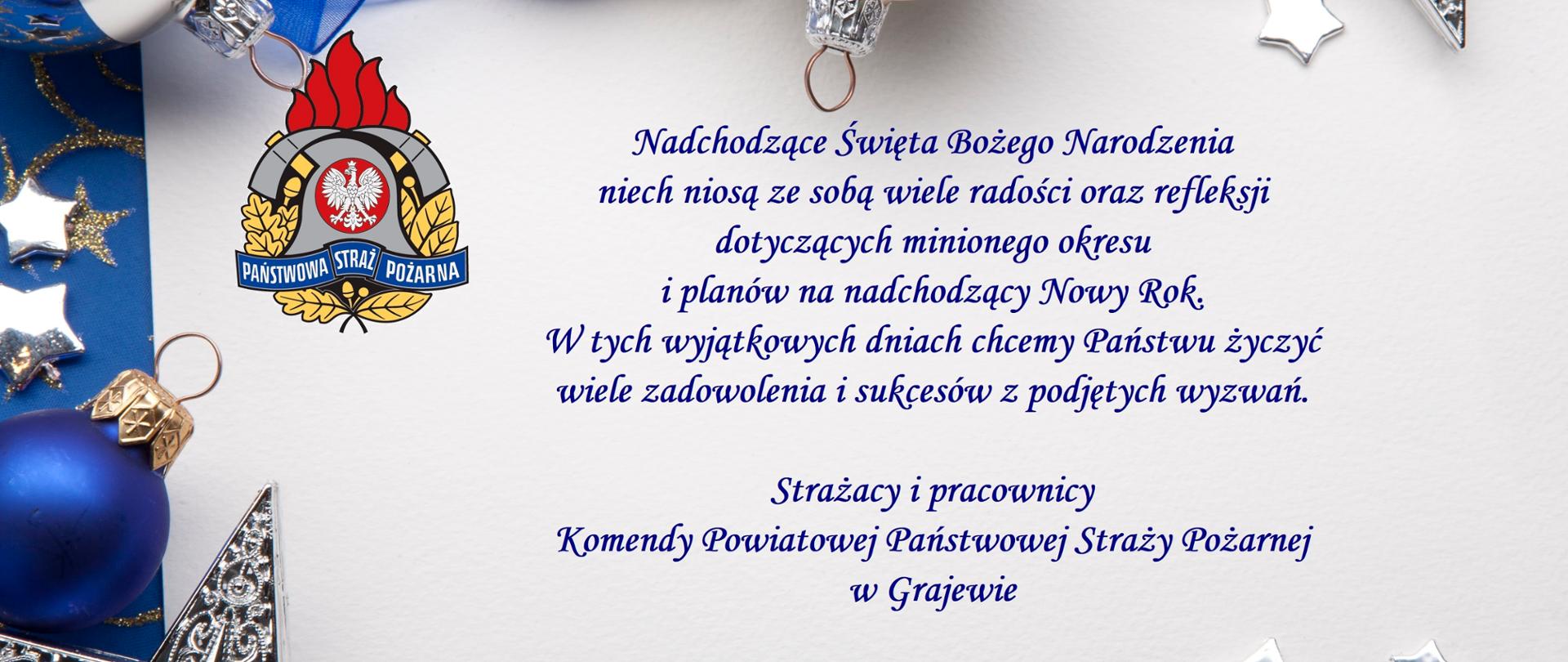 Na zdjęciu białe pole z życzeniami od funkcjonariuszy i pracowników KP PSP w Grajewie, po lewej stronie logo PSP. W koło białego pola niebieskie tło na nim bombki choinkowe w kolorze niebieskim i białym oraz srebrne gwiazdki. 