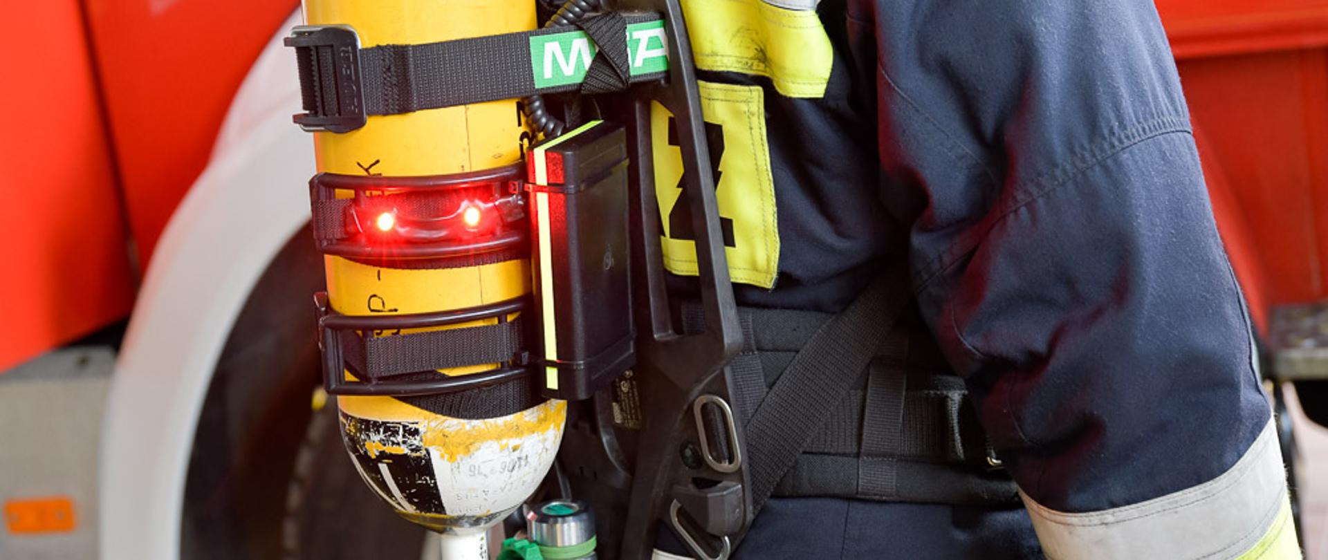 Urządzenie skonstruowane przez inż. Sebastiana Juraszka umieszczone na aparacie ochrony układu oddechowego. Część umieszczona na butli aparatu. Aparat na plecach umundurowanego strażaka.