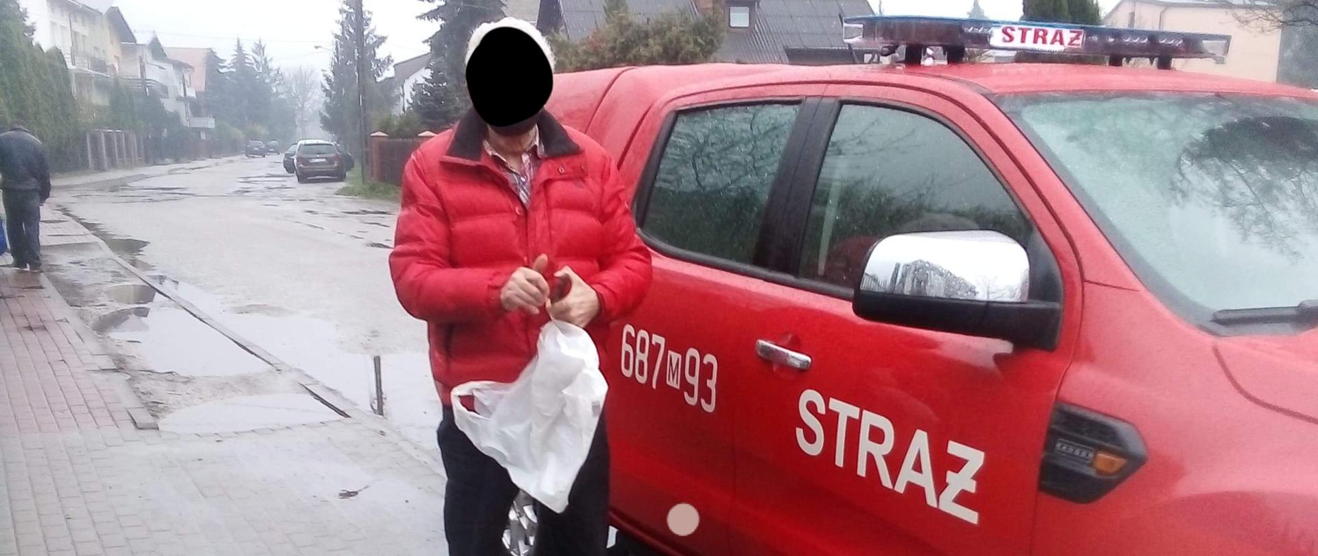 Na pierwszym planie na zdjęciu widać samochód OSP typu pic-up. Do środka wsiada mężczyzna, który ma założoną maseczkę na twarzy. 