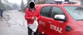 Na pierwszym planie na zdjęciu widać samochód OSP typu pic-up. Do środka wsiada mężczyzna, który ma założoną maseczkę na twarzy. 