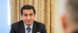 Na zdjęciu siedzący przy stole doradca prezydenta ds. zagranicznych Hikmet Hajiyev. Na stole szklanki, butelki z wodą, materiały. Po prawej stronie widać siedzącego tyłem ministra Tomasz Siemoniaka. W tle widać okno i żółtą kotarę (po prawej stronie).