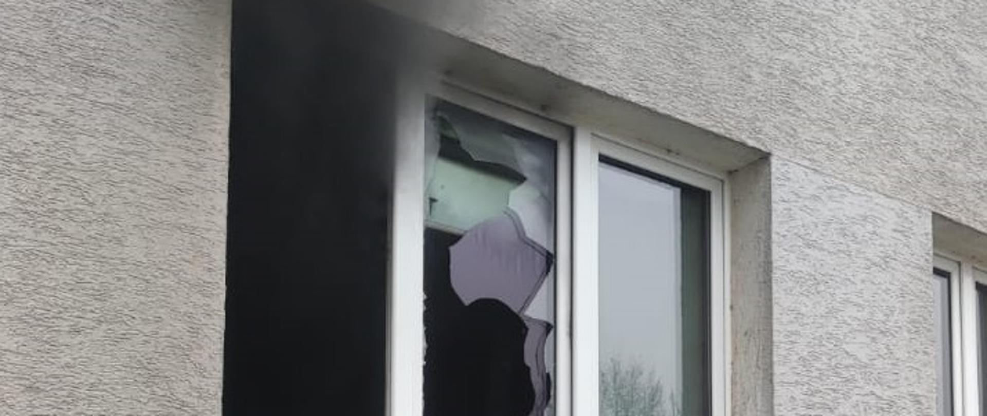 Na zdjęciu wybita szyba w oknie po pożarze i unoszący się dym. 