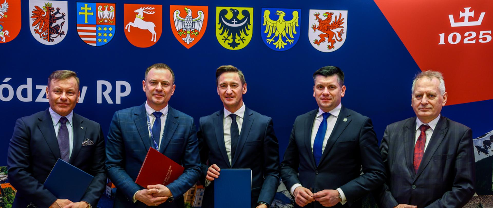 Piotr Borys na Konwencie Marszałków Województw RP w Krakowie na tle ścianki z herbami województw