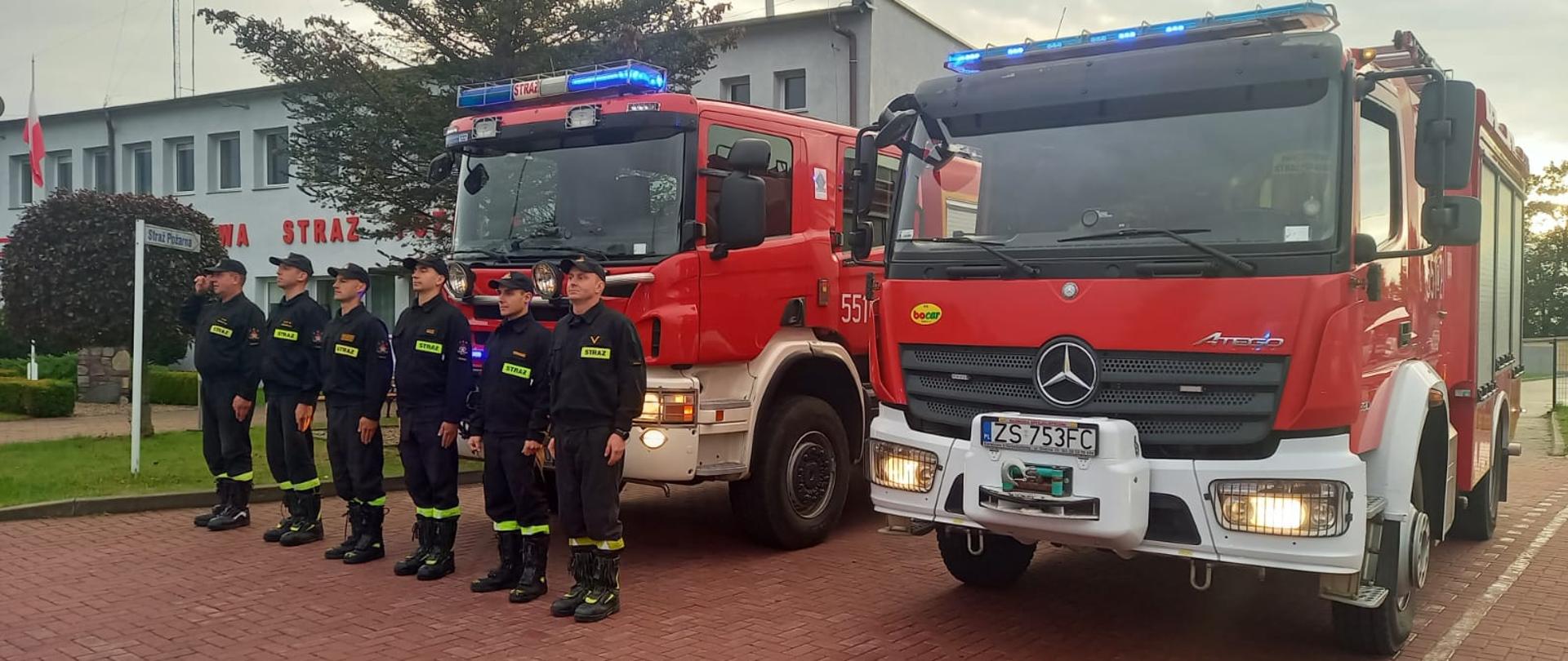 Zdjęcie przedstawia dwa wozy przed budynkiem KP PSP Świdwin z włączonymi światłami a przed nimi stoją na baczność strażacy w rzędzie oddając hołd dla druha z OSP Balice