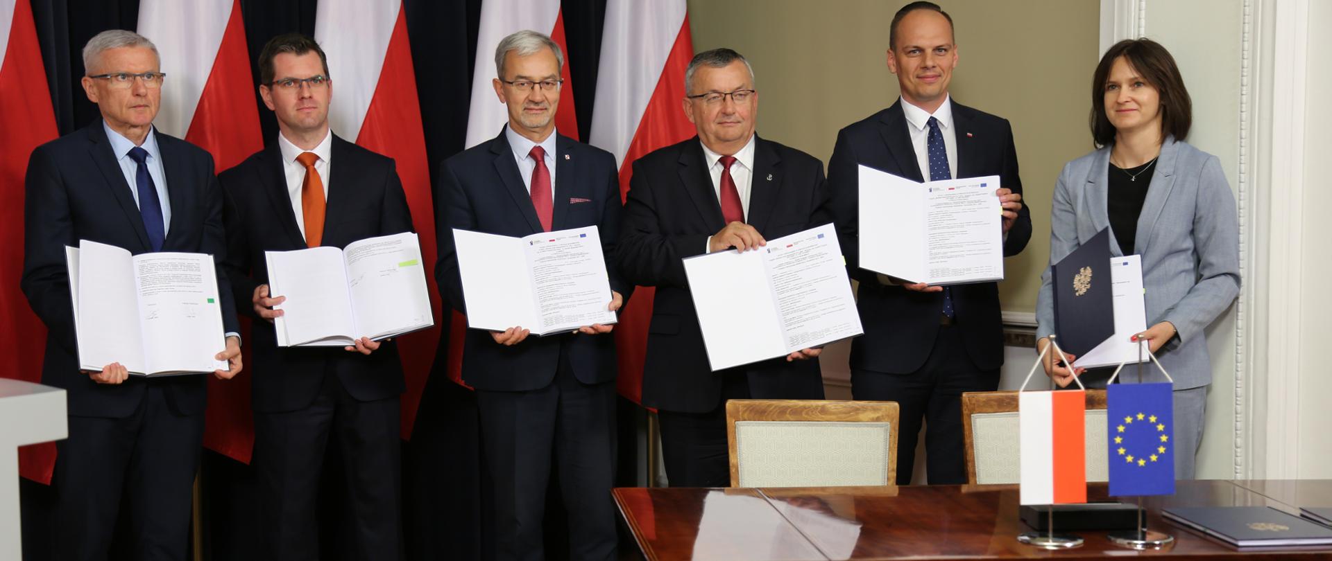 uczestnicy konferencji trzymają otwarte umowy o dofinansowanie z funduszy unijnych