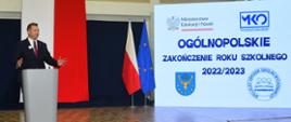 W sali, minister Czarnek stoi i mówi do mikrofonu, za nim na ścianie napis Ogólnopolskie zakończenie roku szkolnego 2022/2023.