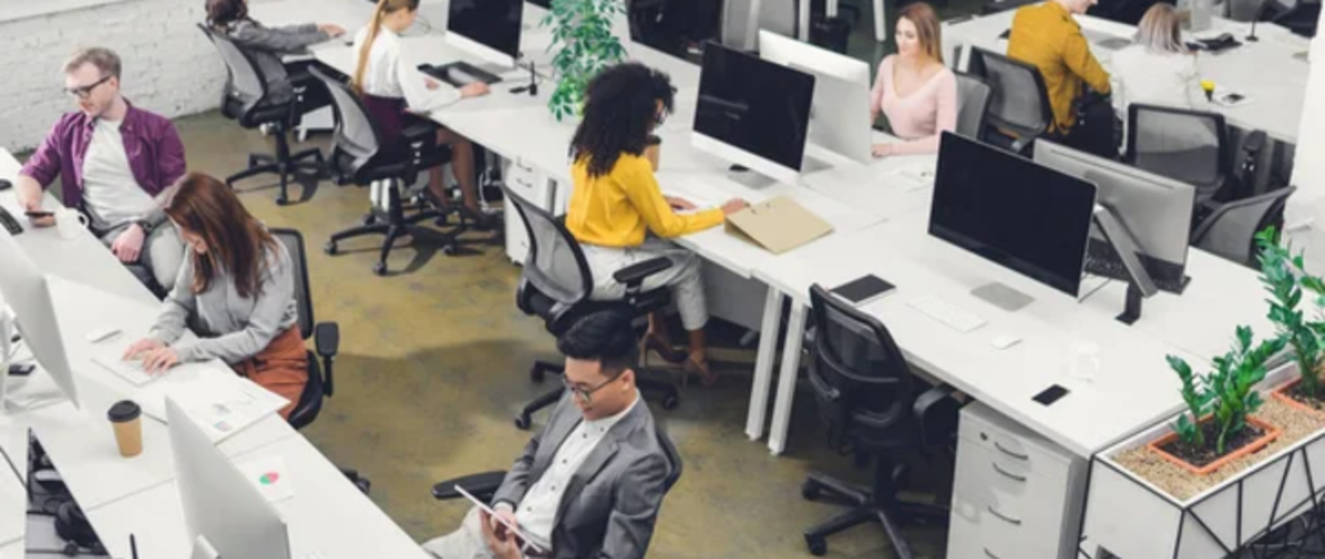 Na zdjęciu znajdują się ludzie pracujący w biurze przy białych biurkach z komputerami.