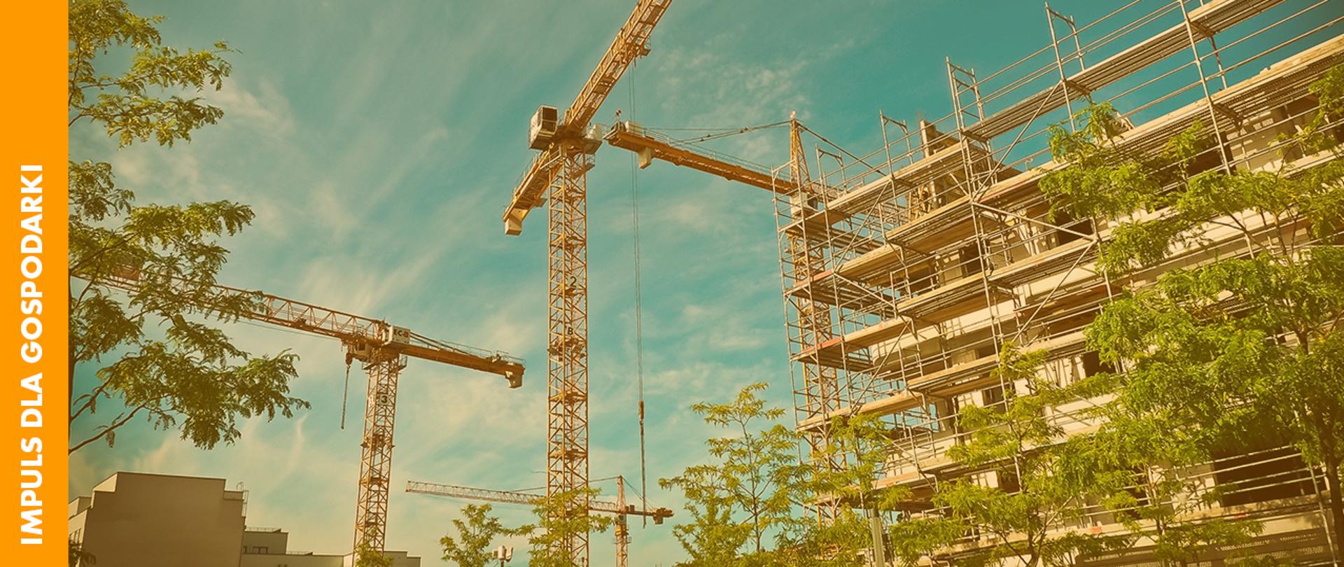 Zdjęcie przestawiające żurawie pracujące na budowie osiedla mieszkaniowego, w otoczeniu drzew. Z lewej strony żółty pasek z białym napisem: Impuls dla gospodarki. 