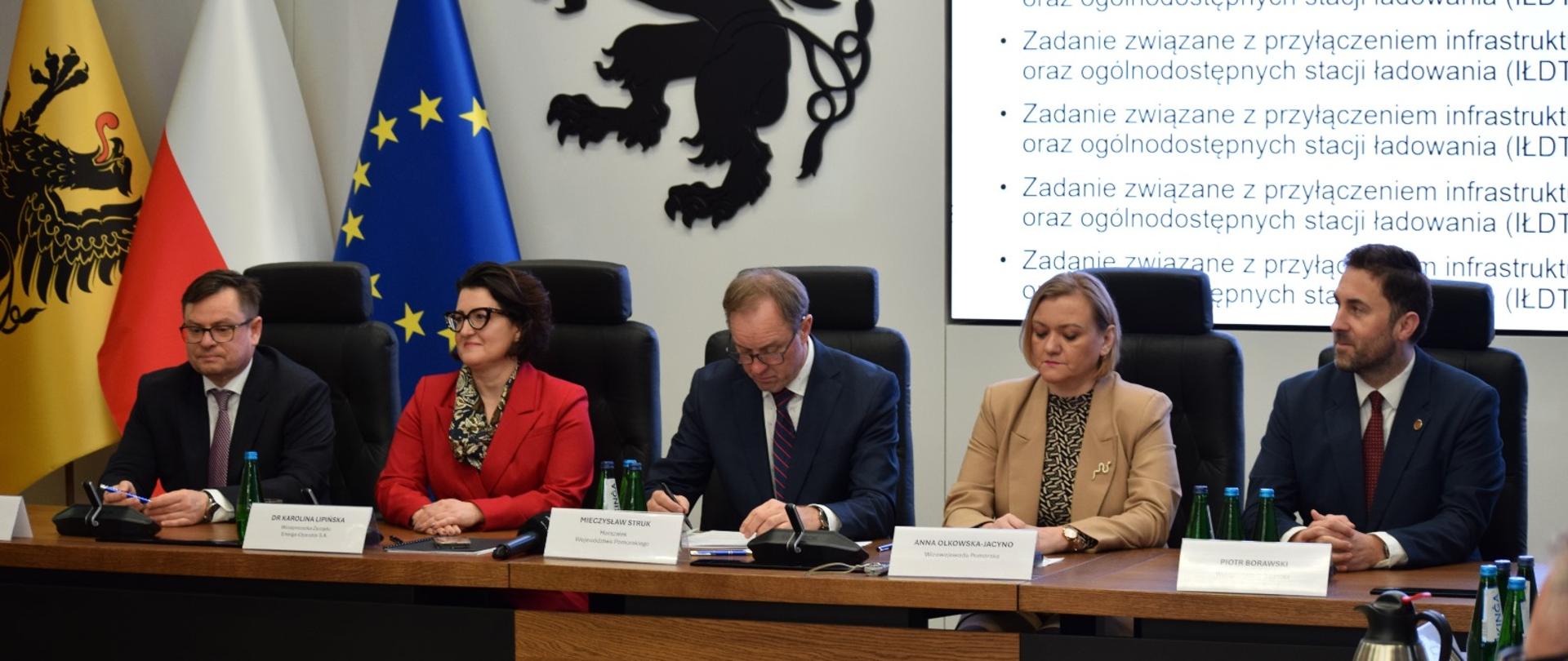 kilka osób siedzi przy biurku i podpisuje umowę