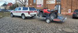 Na zdjęciu widać quada na przyczepce podpiętej do białego samochodu rozpoznawczo-ratowniczego typu pickup