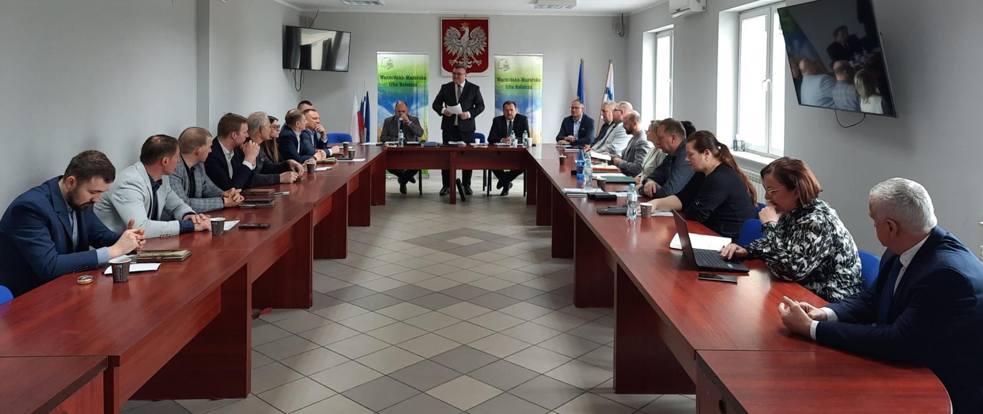 Wystąpienie Przewodniczącego Rady Powiatu – Pana Marcina Sarnowskiego. Uczestnicy Rady Powiatu, słuchający wystąpienia siedzą przy stołach ustawionych w literę U.