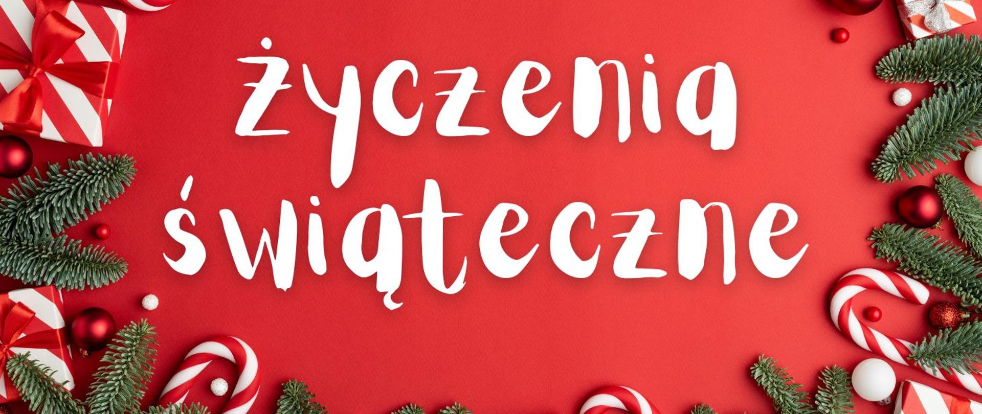 Na środku duży biały napis odręcznym krojem: „Życzenia świąteczne”. Ramkę tworzą zielone gałązki świerku, czerwono-białe laski cukrowe, bombki oraz zapakowane prezenty rozmieszczone wzdłuż krawędzi grafiki, całość na czerwonym tle