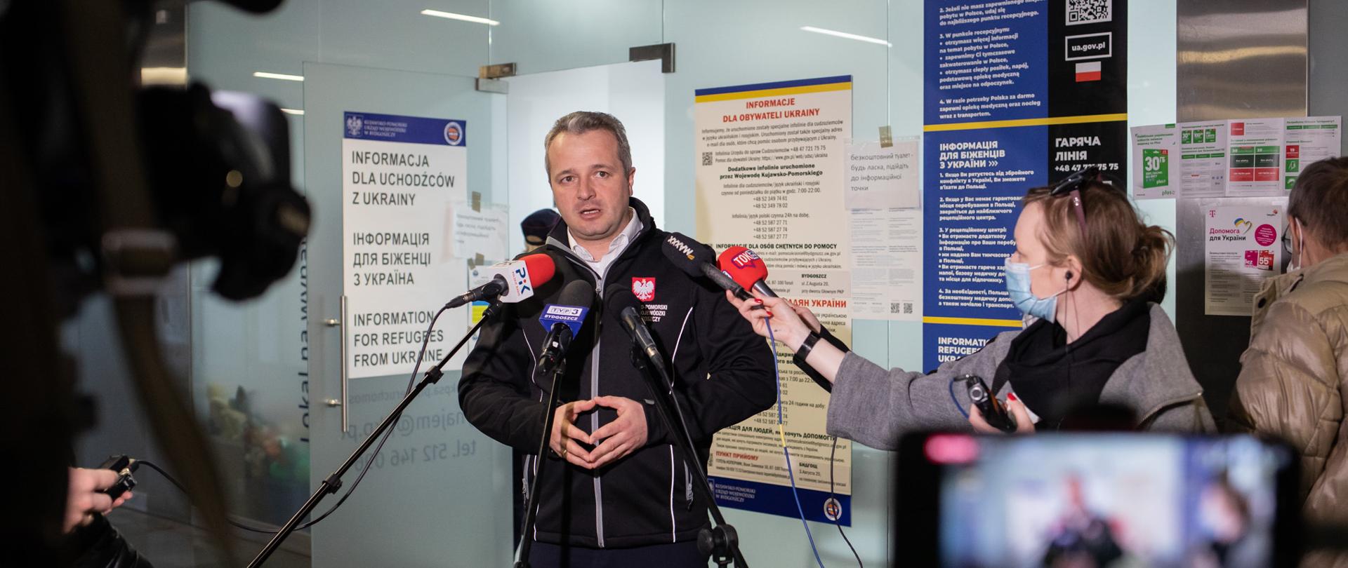 Mężczyzna stojący przed mikrofonami i dziennikarzami i wypowiadający się 