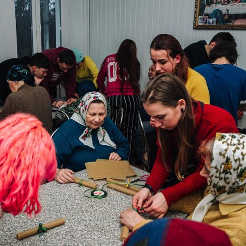 Grupa kilkunastu osób zajęta przygotowywaniem rulonów związanych zieloną wstążką.