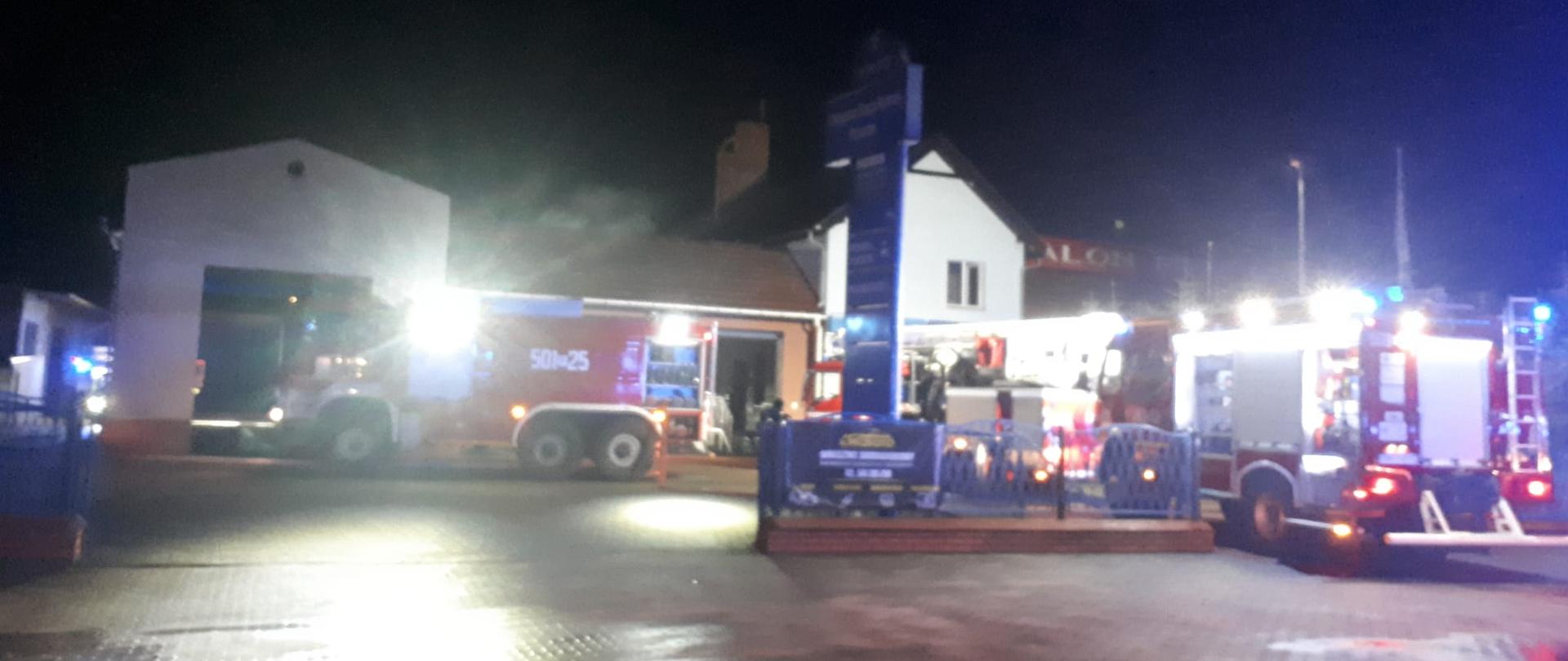 Na zdjęciu samochody pożarnicze podczas działań gaśniczych. W tle budynek handlowo - usługowy, który uległ zapaleniu.