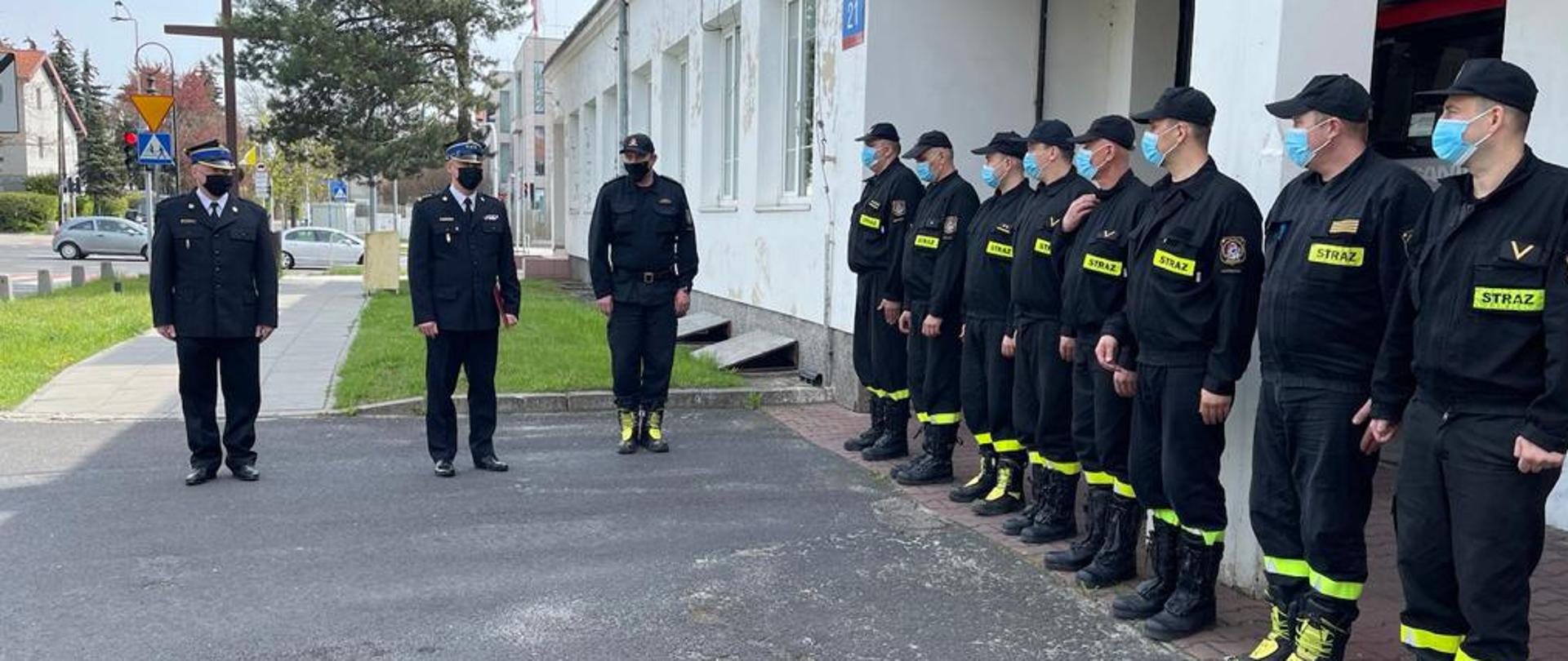 Uroczysta zbiórka przez Jednostką Ratowniczo Gaśniczą nr 14. Po prawo stoi zmiana służbowa ubrana w umundurowanie koszarowe. Przed pododdziałem stoją Komendant Miejski Państwowej Straży Pożarnej m.st. Warszawy, nowy Dowódca Jednostki Ratowniczo-Gaśniczej nr 14 oraz jego zastępca. 