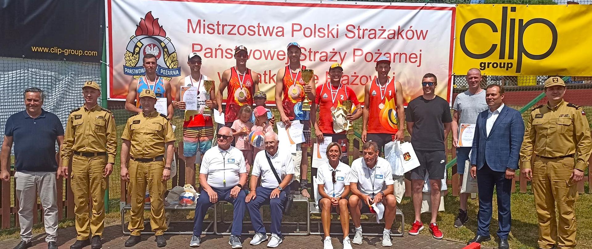 Grupowe zdjęcie zawodników i osób zaproszonych, za nimi napis Mistrzostwa Polski Strażaków PSP
