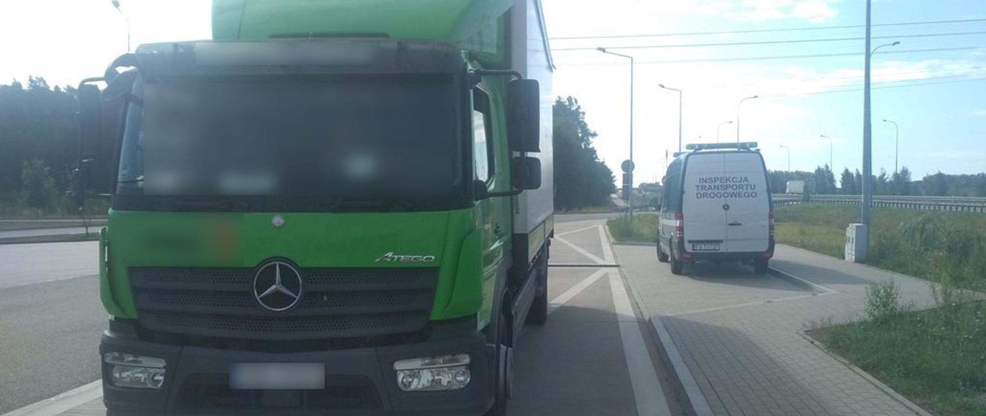 Na pierwszym planie (od lewej): przód i lewy bok samochodu ciężarowego - solówki. W tle: stojący obok zatoki kontrolnej oznakowany furgon inspekcji Transportu Drogowego.