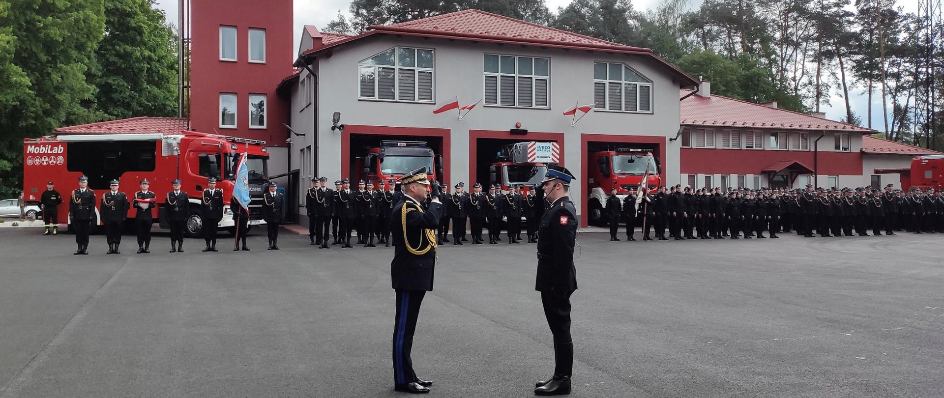 Na zdjęciu widzimy zastępcę komendanta głównego oraz prowadzącego uroczystość oficera oddającego honory w tle widzimy pododdziały straży pożarnej.