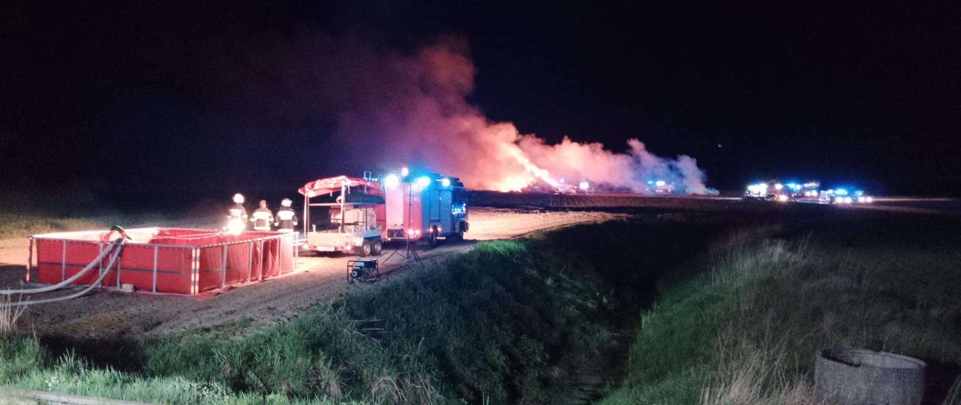 Na zdjęciu an pierwszym planie widać bufor wodny stworzony w oparciu o zbiornik wody, w tle palący się stóg.