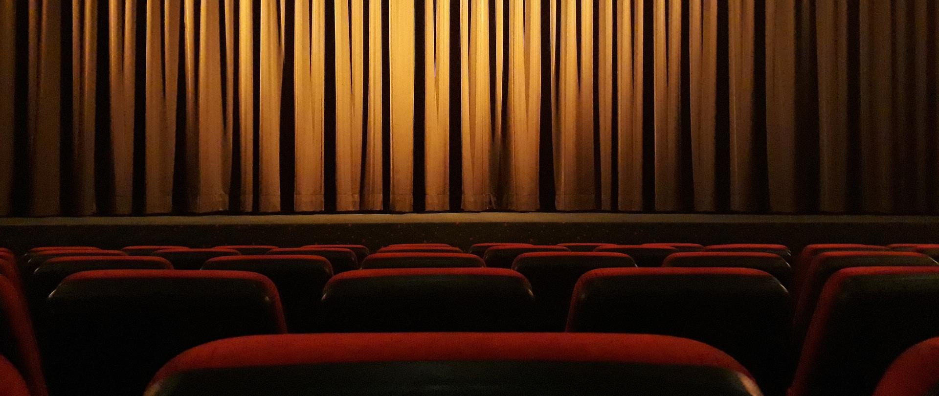 Na dole zdjęcia widoczne w kolorze czerwonym oparcia widowni, w dali zasłonięta kurtyna na scenie