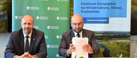 Na zdjęciu na tle banera z logo Narodowego Funduszu Ochrony Środowiska i Gospodarki Wodnej siedzą przy stole od lewej Zastępca Prezesa Narodowego Funduszu Ochrony Środowiska i Gospodarki Wodnej Robert Gajda i Prezes Zarządu Przedsiębiorstwa Wodociągów i Kanalizacji Sławomir Pszenny. Zdjęcie przedstawia moment podpisania umowy. 