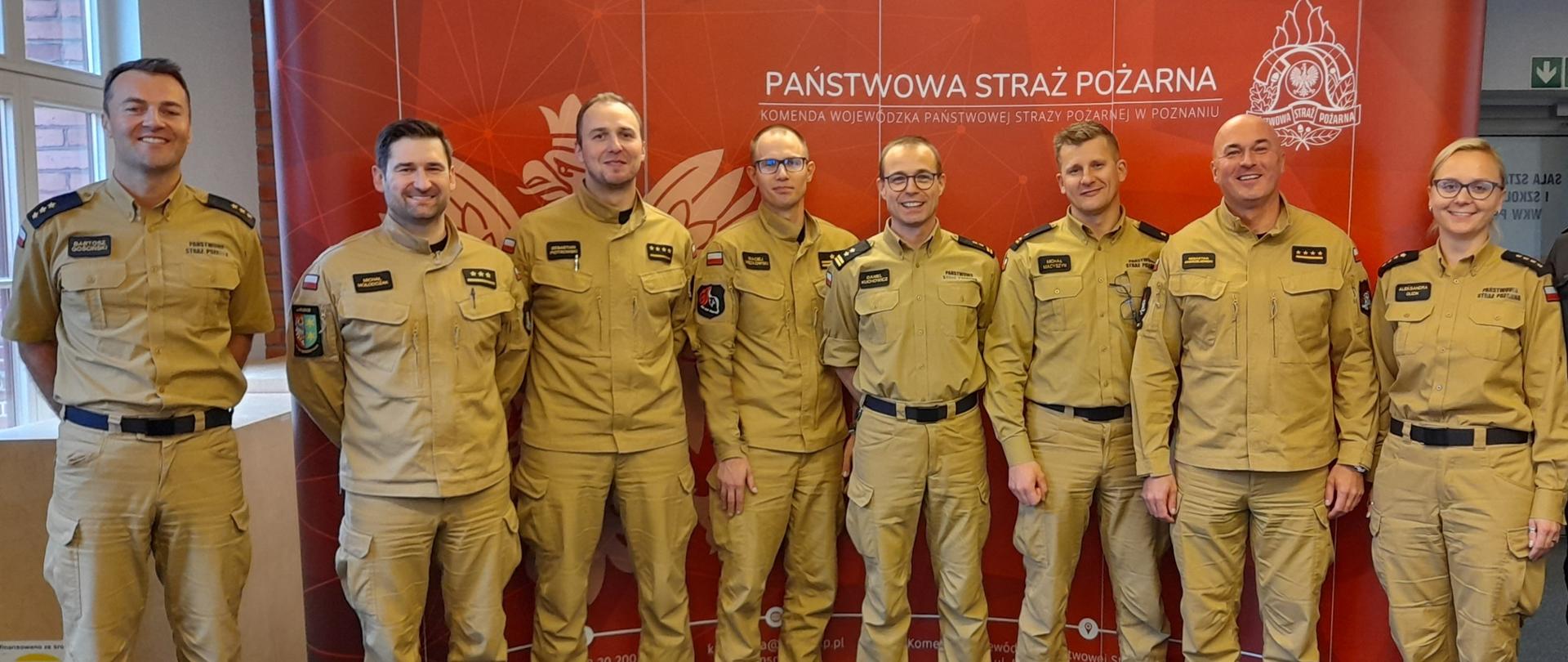 zdjęcie grupowe strażaków w pisakowych mundurach , w tle czerwony baner