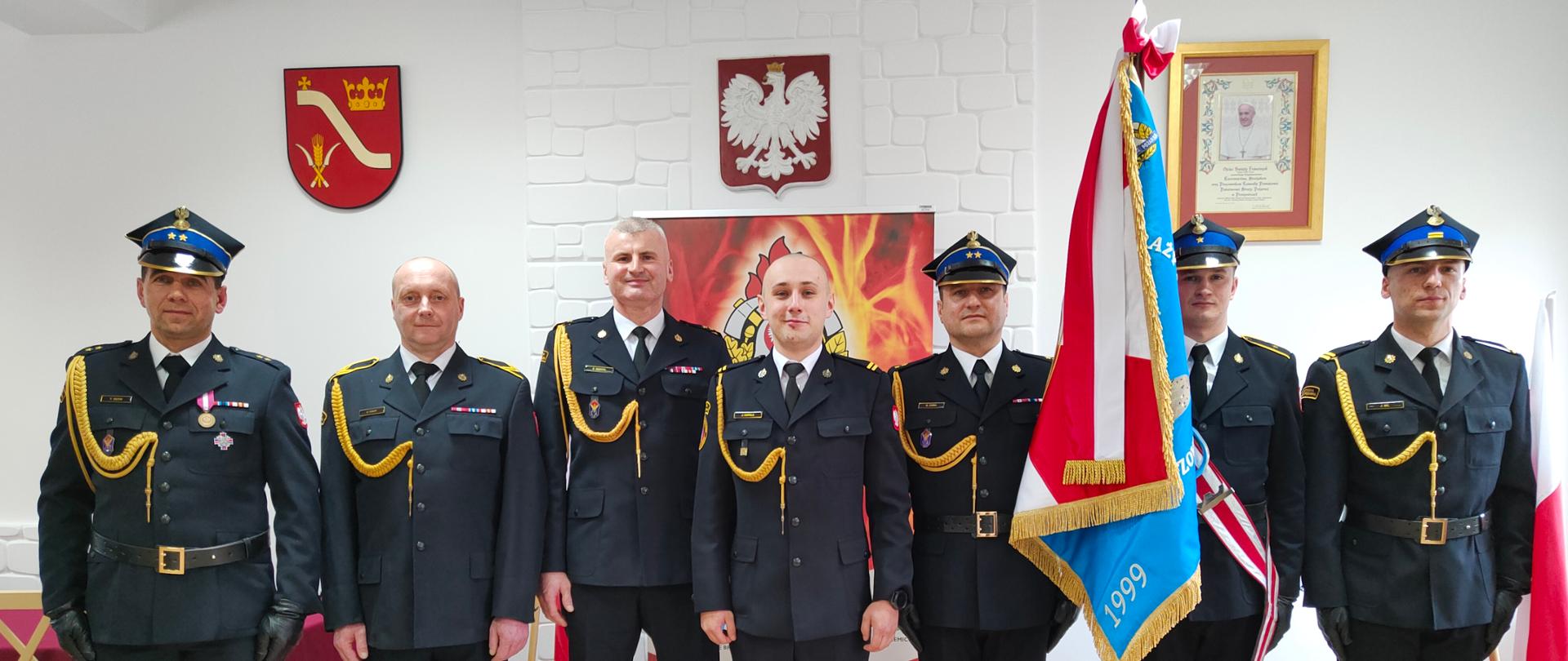 Strażacy w mundurach galowych pozują ze sztandarem do zdjęcia 
