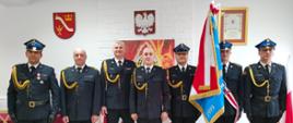 Strażacy w mundurach galowych pozują ze sztandarem do zdjęcia 