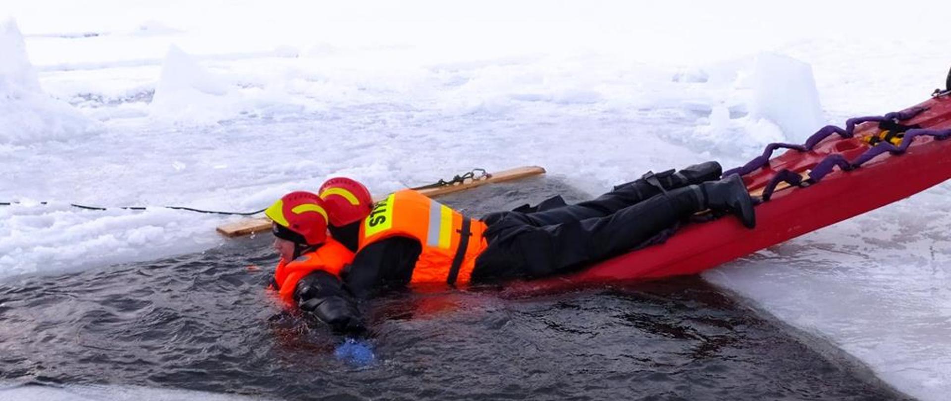 Strażak zabezpieczony na saniach lodowych podejmuje z wody osobę pod którą załamał się lód