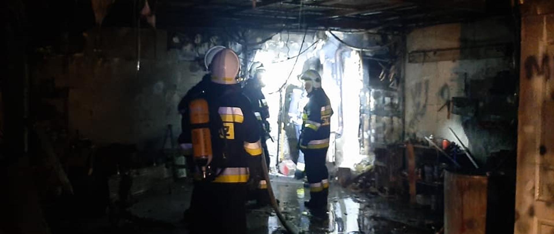 Widać wnętrze spalonego garażu, w środku jest trzech strażaków