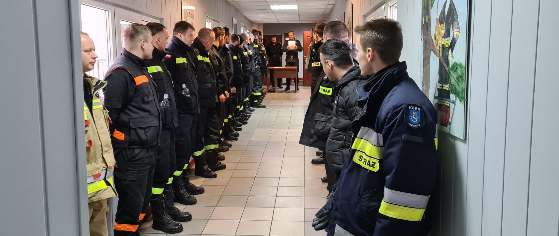 druhowie OSP podczas Szkolenia kierowcy-konserwatora OSP stoją w pomieszczeniu w dwóch szeregach, w tle funkcjonariusze PSP