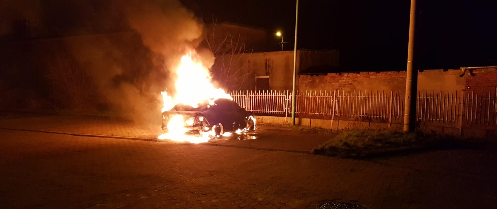 W Lubsku na parkingu przy ogrodzeniu pali się samochód osobowy. Samochód pali się w całości, płomienie sięgają dwóch metrów. W bliskiej odległości znajduje się budynek.