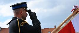 Strażak salutuje przy rozwinięty, sztandarze.