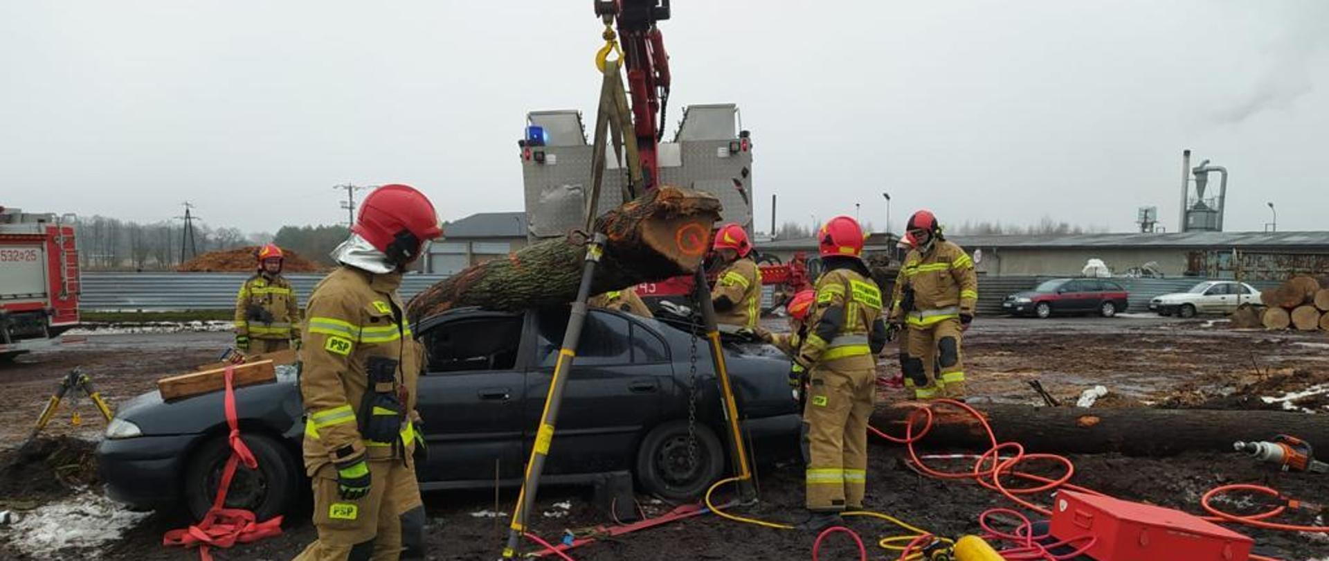 Strażacy stabilizują kłody drewna, które powaliły się na samochód 