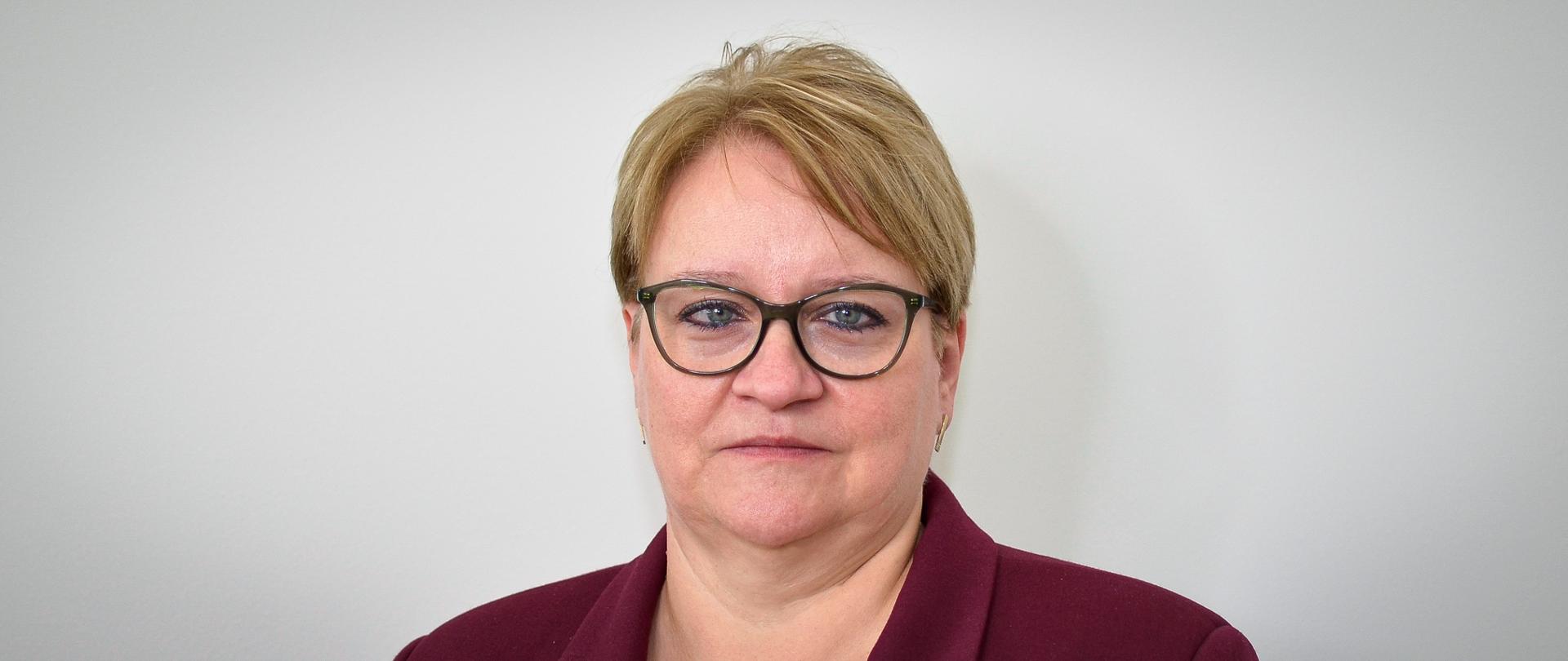 Kobieta w bordowej marynarce, w okularach, z krótkimi włosami