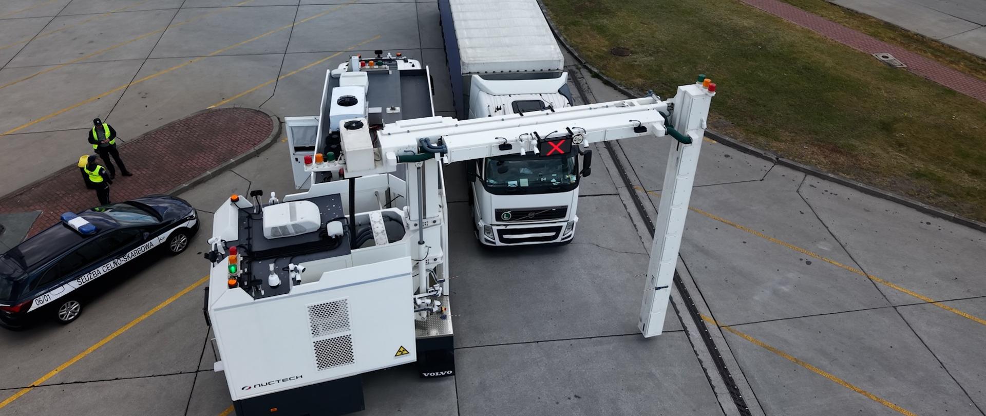 Skaner mobilny do którego podjeżdża ciężarówka. Z boku radiowóz Służby Celno-Skarbowej i dwóch funkcjonariuszy.