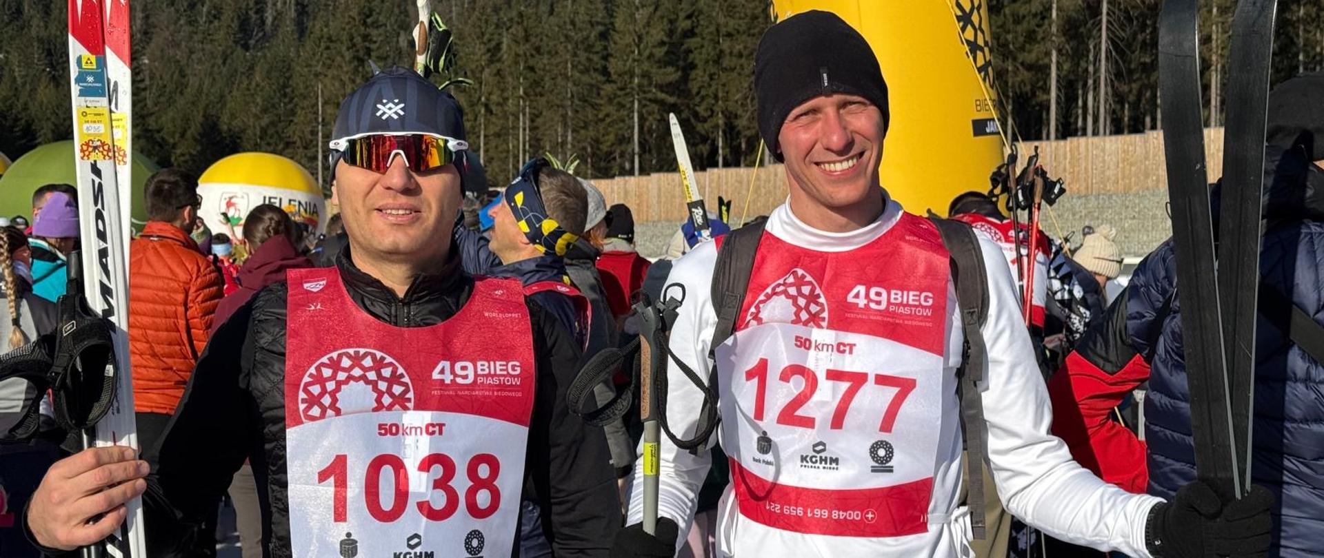 Strażacy z KP Starogard na pamiątkowym zdjęciu z nartami, w tle las i inni uczestnicy biegu narciarskiego. 