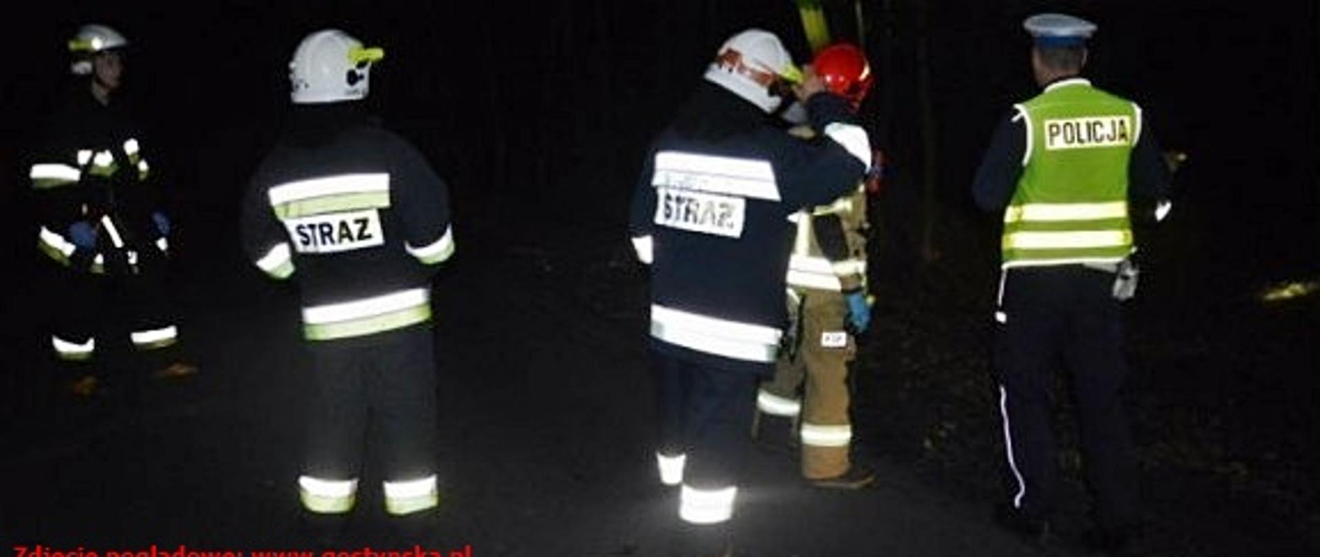 Zdjęcie strażaków i policjanta w trakcie poszukiwań. Zjęcie wykonane w nocy